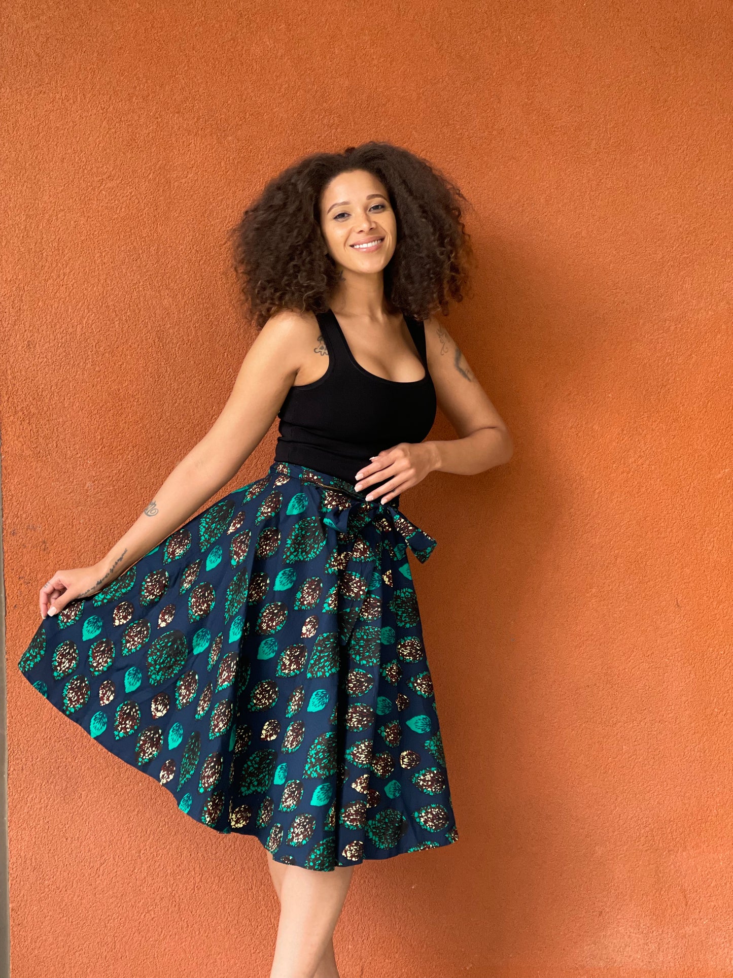 Model wearing Fea Reversible Wrap Skirt – high-waist maxi wrap skirt with African peacock-print on one side and solid black cotton on the reverse, tie waist.